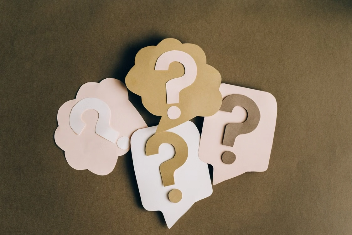Paper speech bubbles with question marks on a surface
