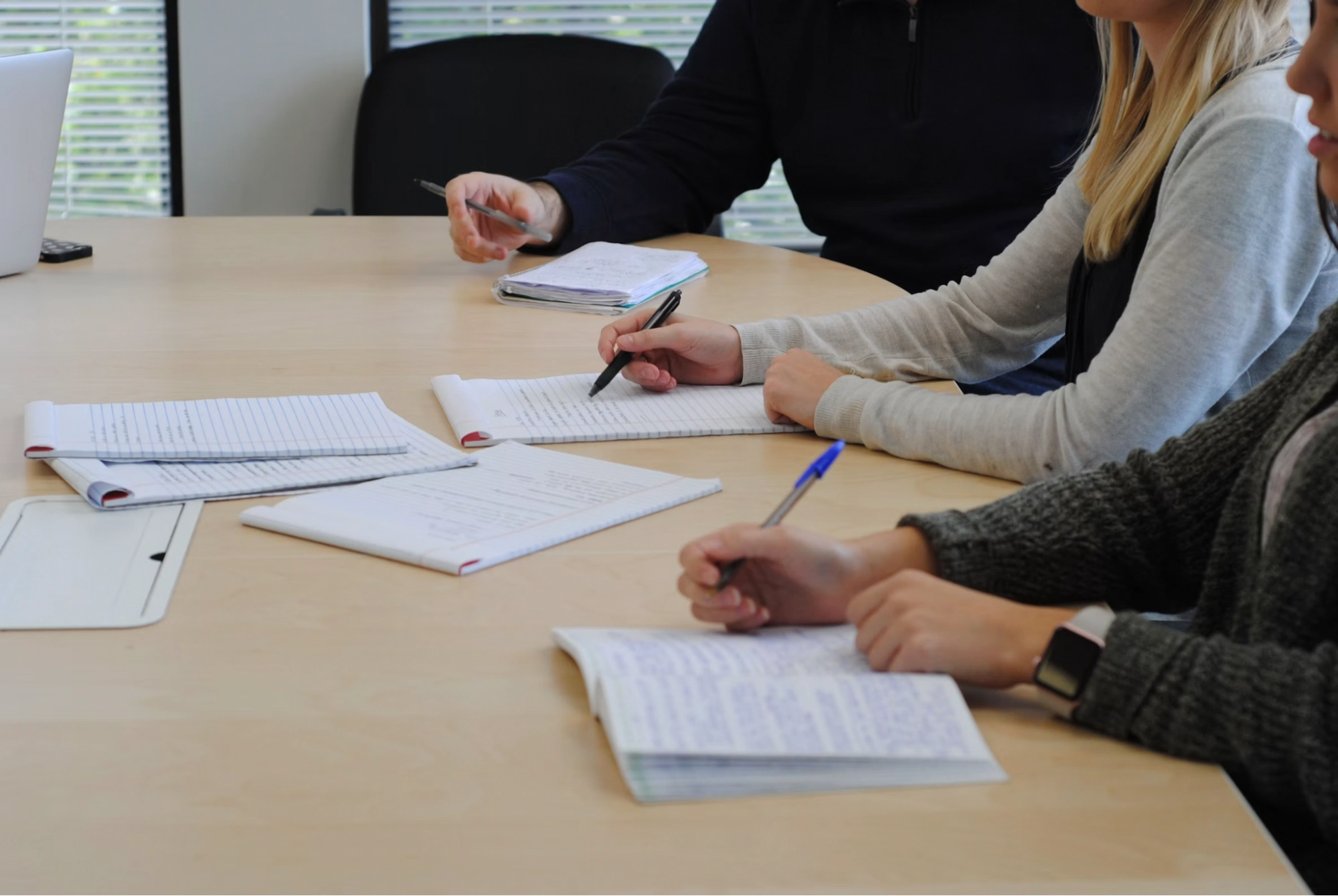 People sitting at a wooden table taking notes